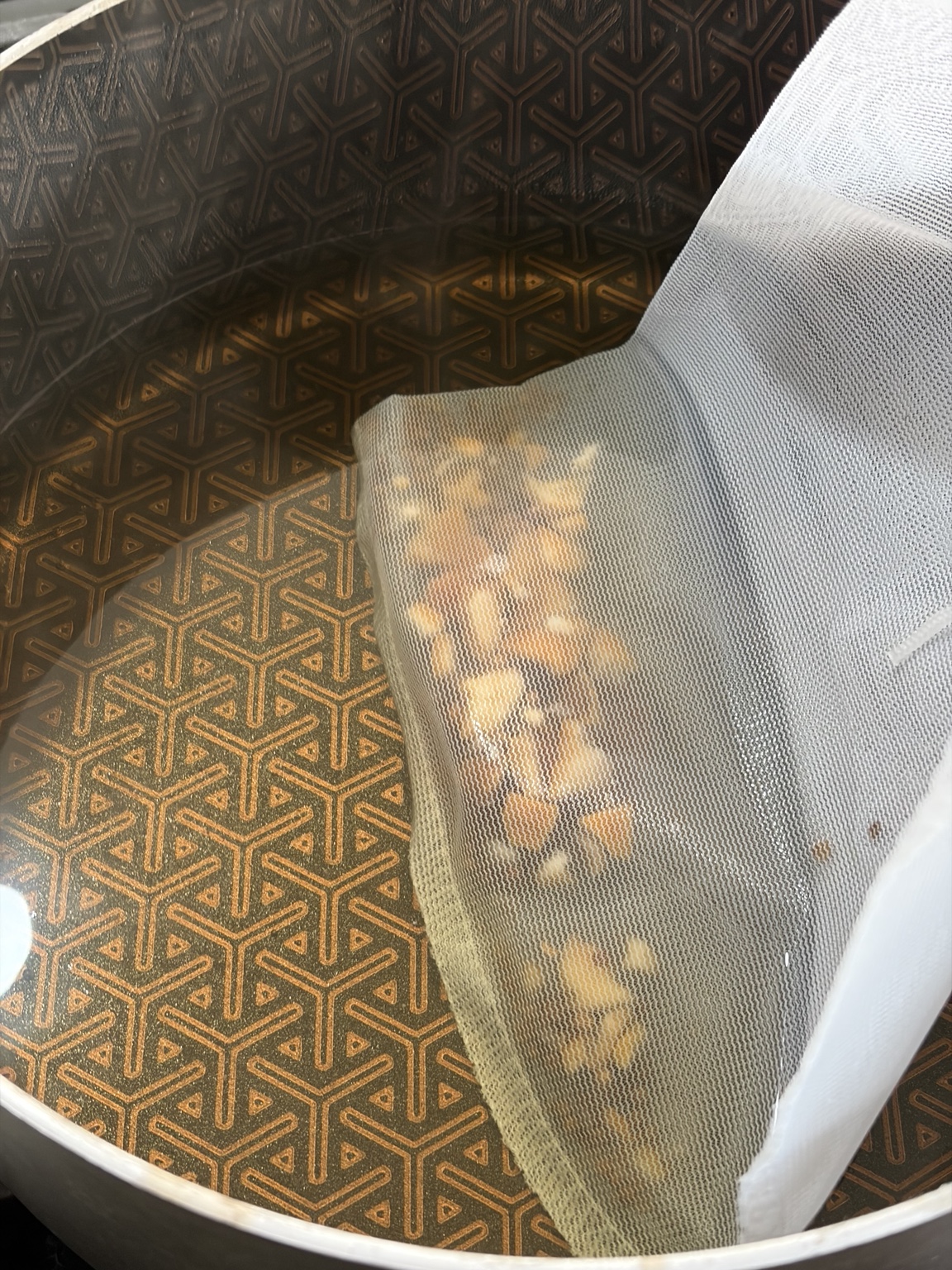 Coriander and bitter orange peel steeping in a nylon mesh bag in one liter of hot water